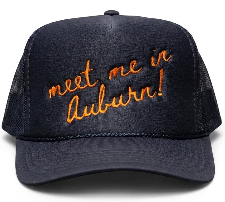 A dark navy blue trucker hat with orange embroidered text reading 'meet me in Auburn!' on the front panel, shown against a plain white background.