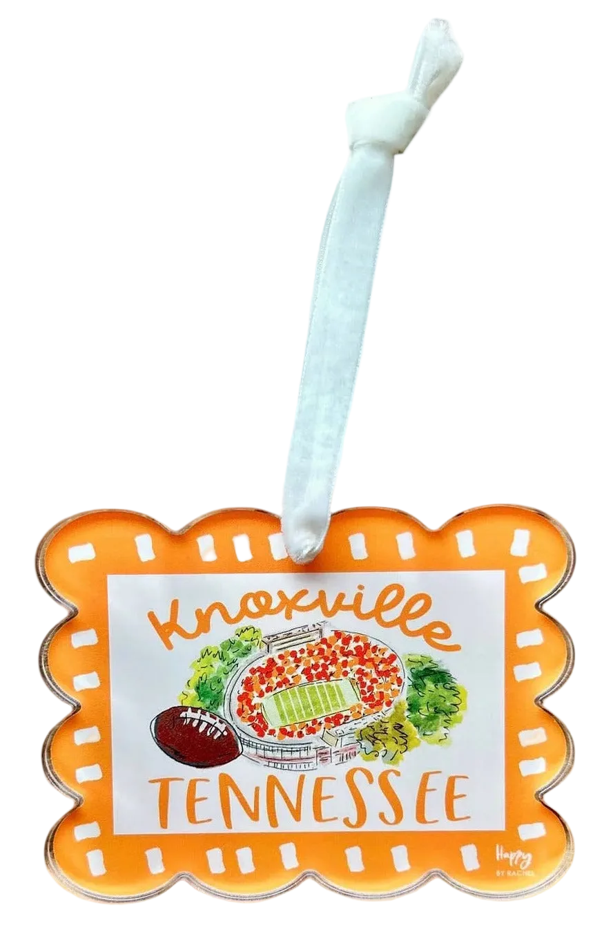 An orange and white Knoxville Tennessee football ornament with a white hanging ribbon, featuring a football field illustration in the center.