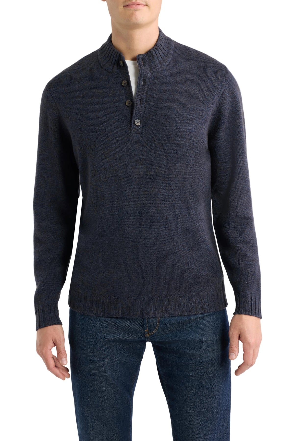 A man wearing a dark navy blue knit sweater with a three-button placket and a mock neck collar, paired with dark blue jeans, against a light gray background.