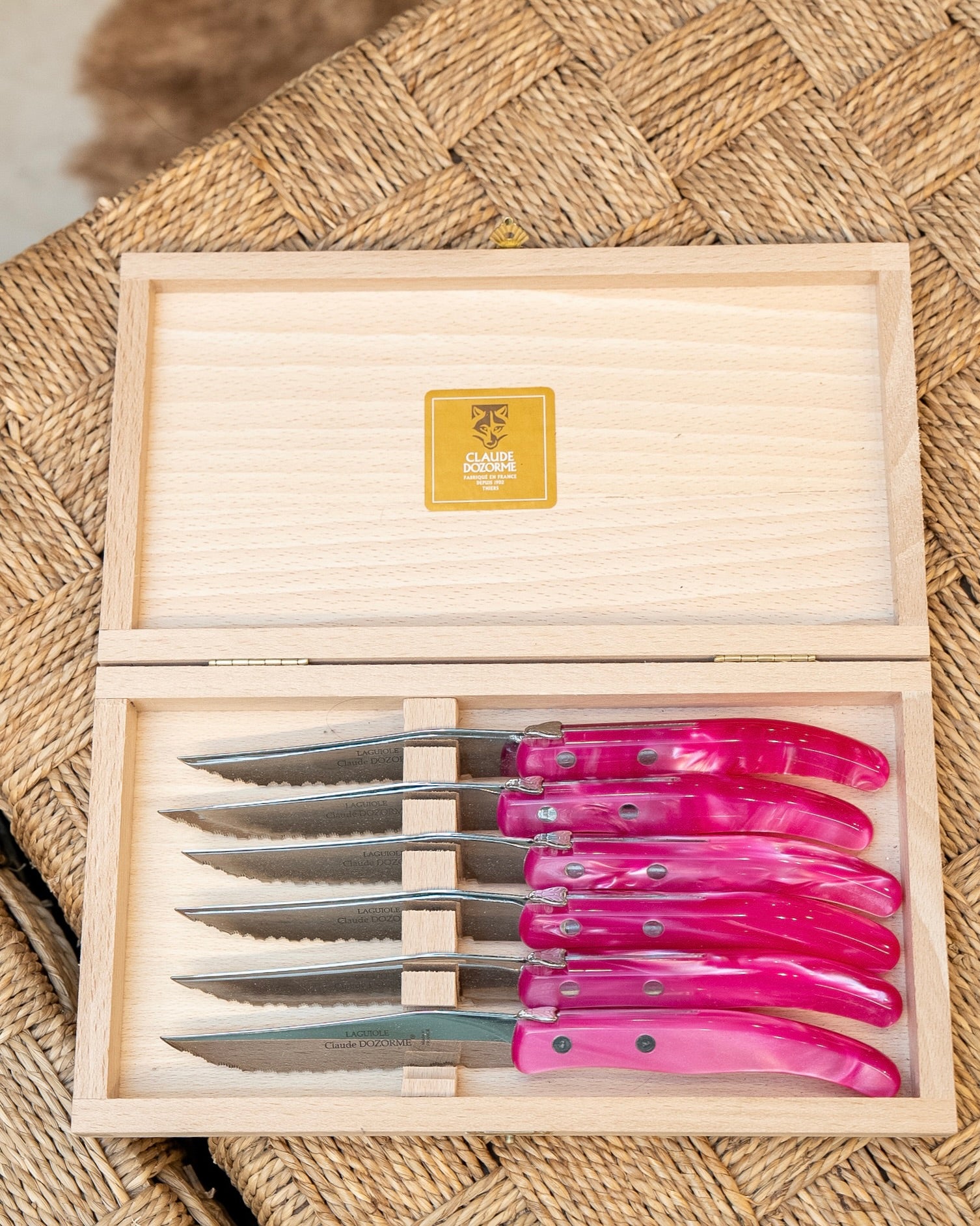 Set of pink-handled knives in a wooden box on a woven surface