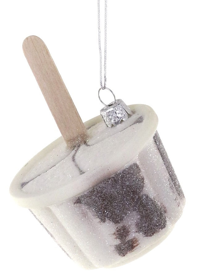 A novelty Christmas ornament shaped like a popsicle, featuring a white and silver glittery frozen body with a dark chocolate swirl, a light wood stick, and a silver hanging loop on a white background.