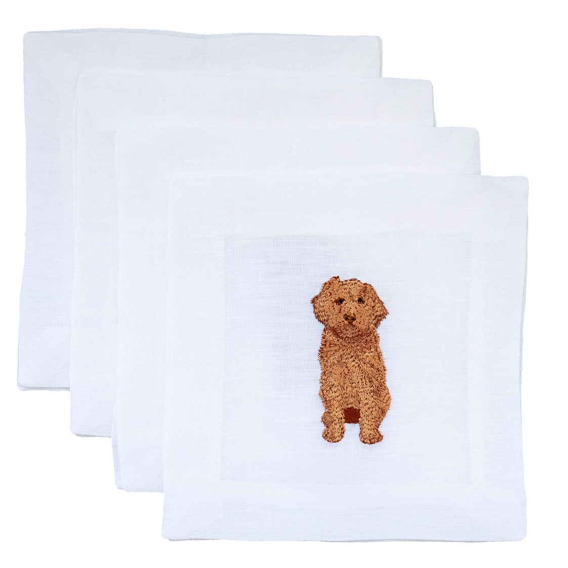 A set of four white cocktail napkins with a central embroidered image of a golden doodle dog on each.