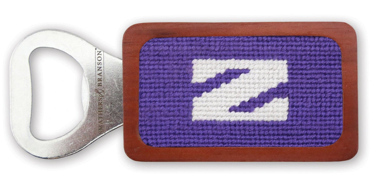 A wooden bottle opener with a purple and white embroidered 'Z' design on the front, set against a plain white background.