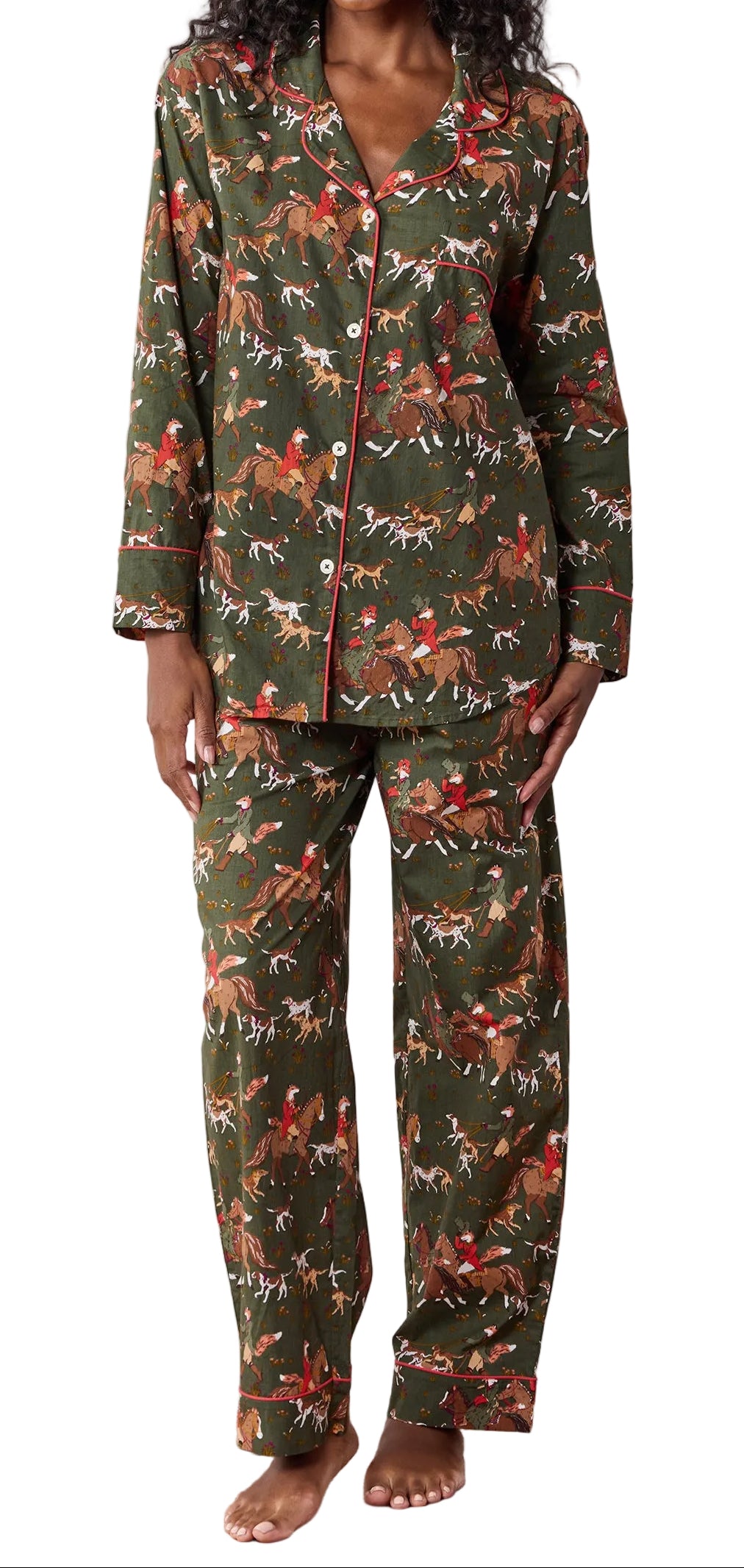 A woman stands barefoot against a plain light wall wearing a matching pajama set with a woodland deer print in olive green, brown, and rust red tones.