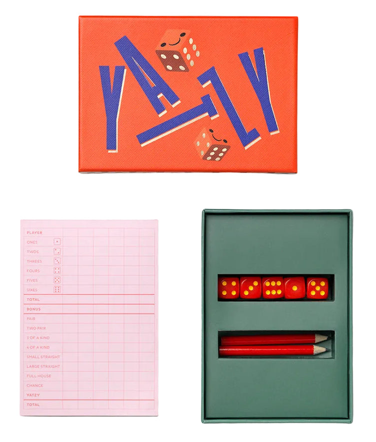 A YAZZY board game set arranged on a light gray background, including an orange game box with blue lettering, a pink score tracker sheet, and an open dark green box containing red dice and red pencils.