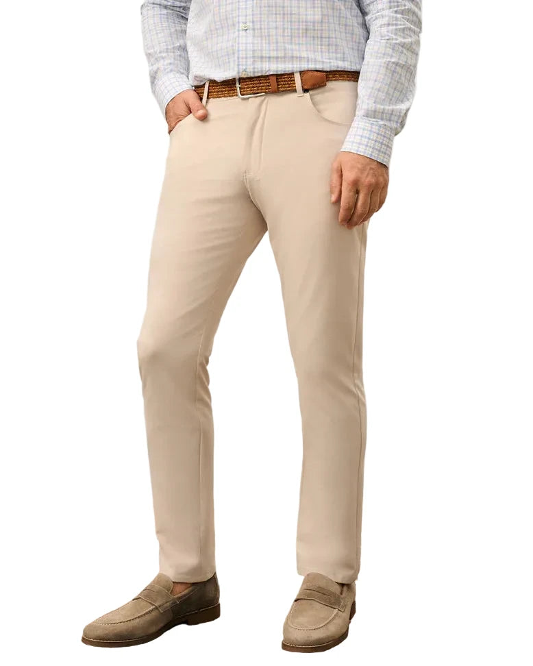 Person wearing beige pants and brown shoes standing on a patterned rug with a plant in the background.