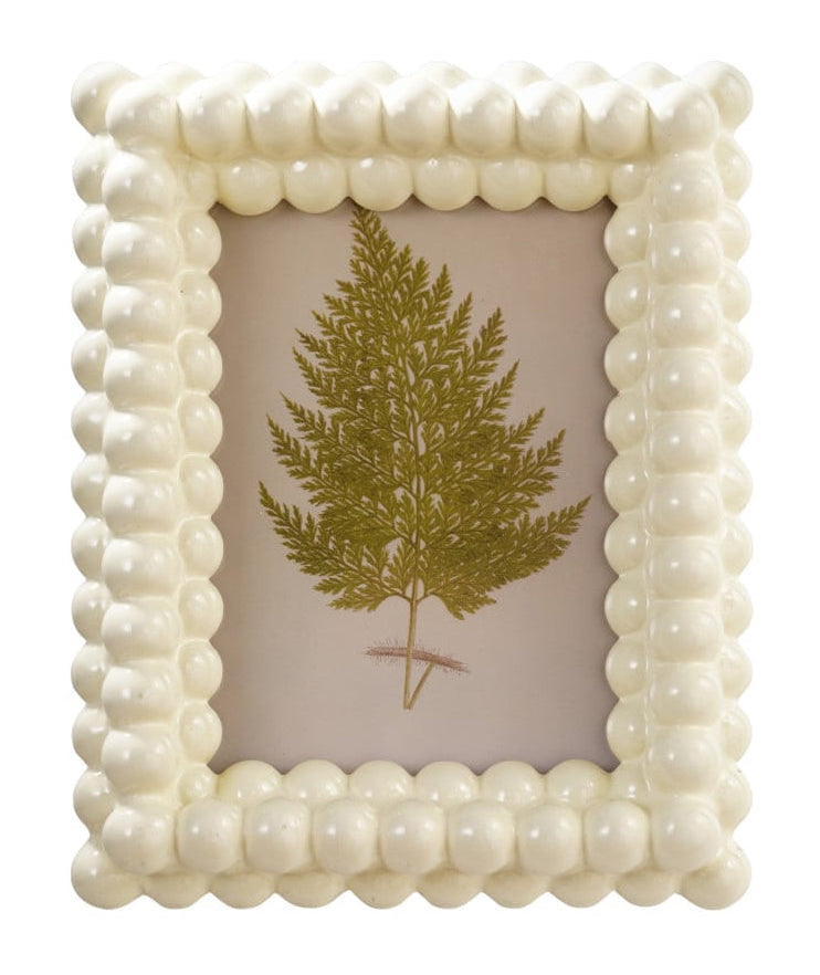A small square decorative picture frame with a cream-colored beaded border, holding a gold glitter fern illustration on a light pink background.