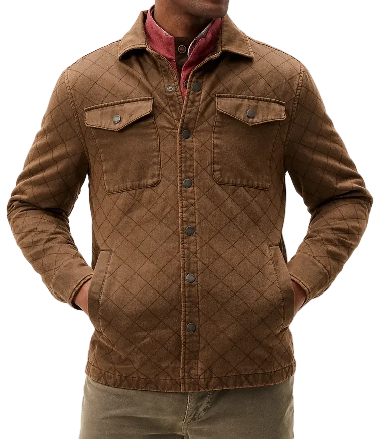 A man wearing a brown diamond-quilted corduroy jacket over a red collared shirt and olive pants, standing against a light gray studio background.