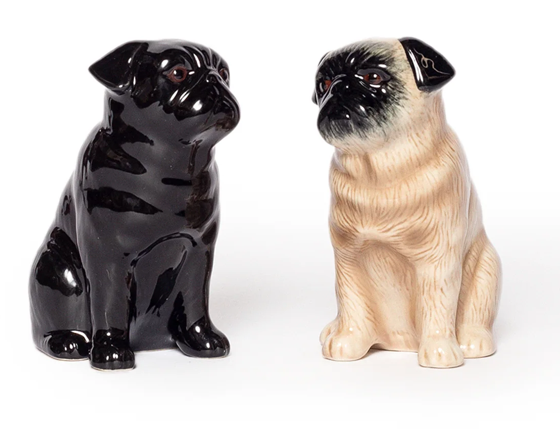 Two ceramic pug dog figurines, one black and one beige, on a white background.