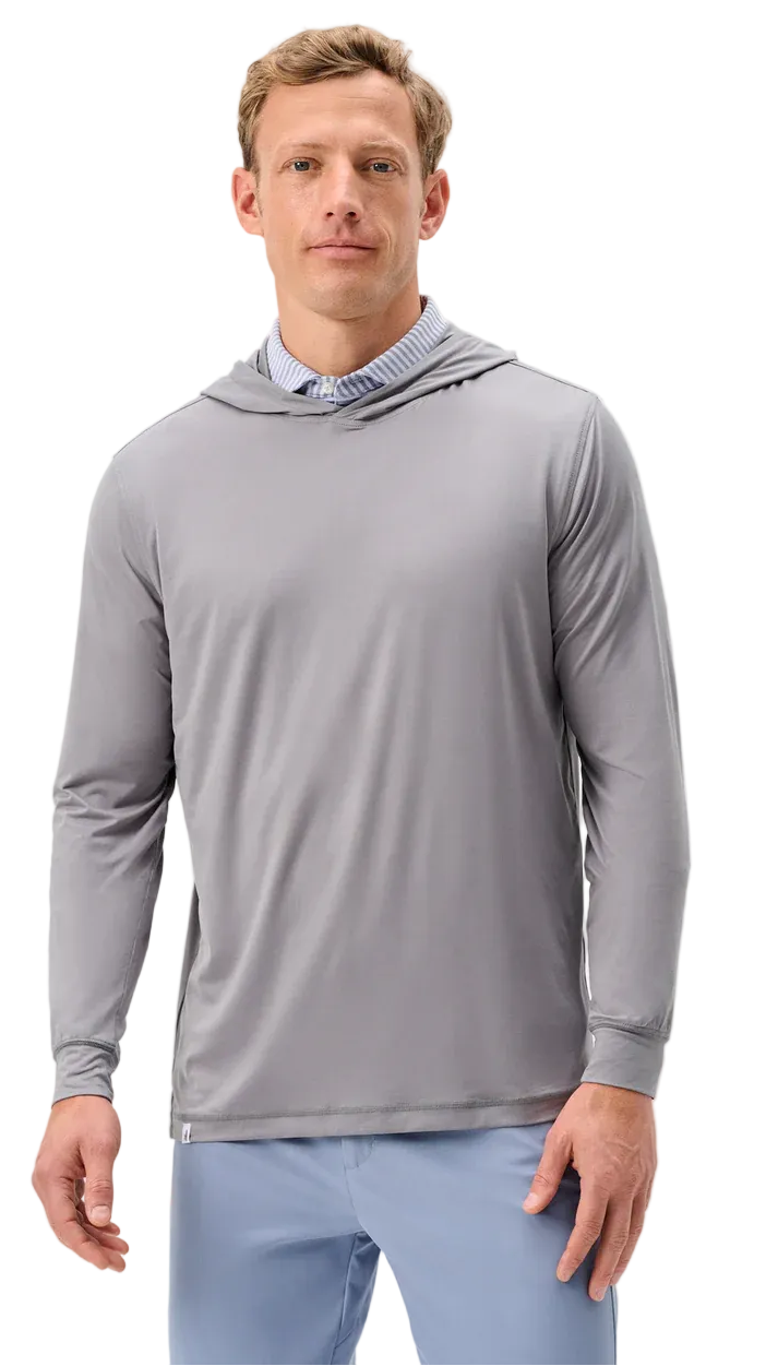 A man wearing a light gray long-sleeve performance hoodie over a blue striped collared shirt and light blue pants, photographed against a plain light gray studio background.