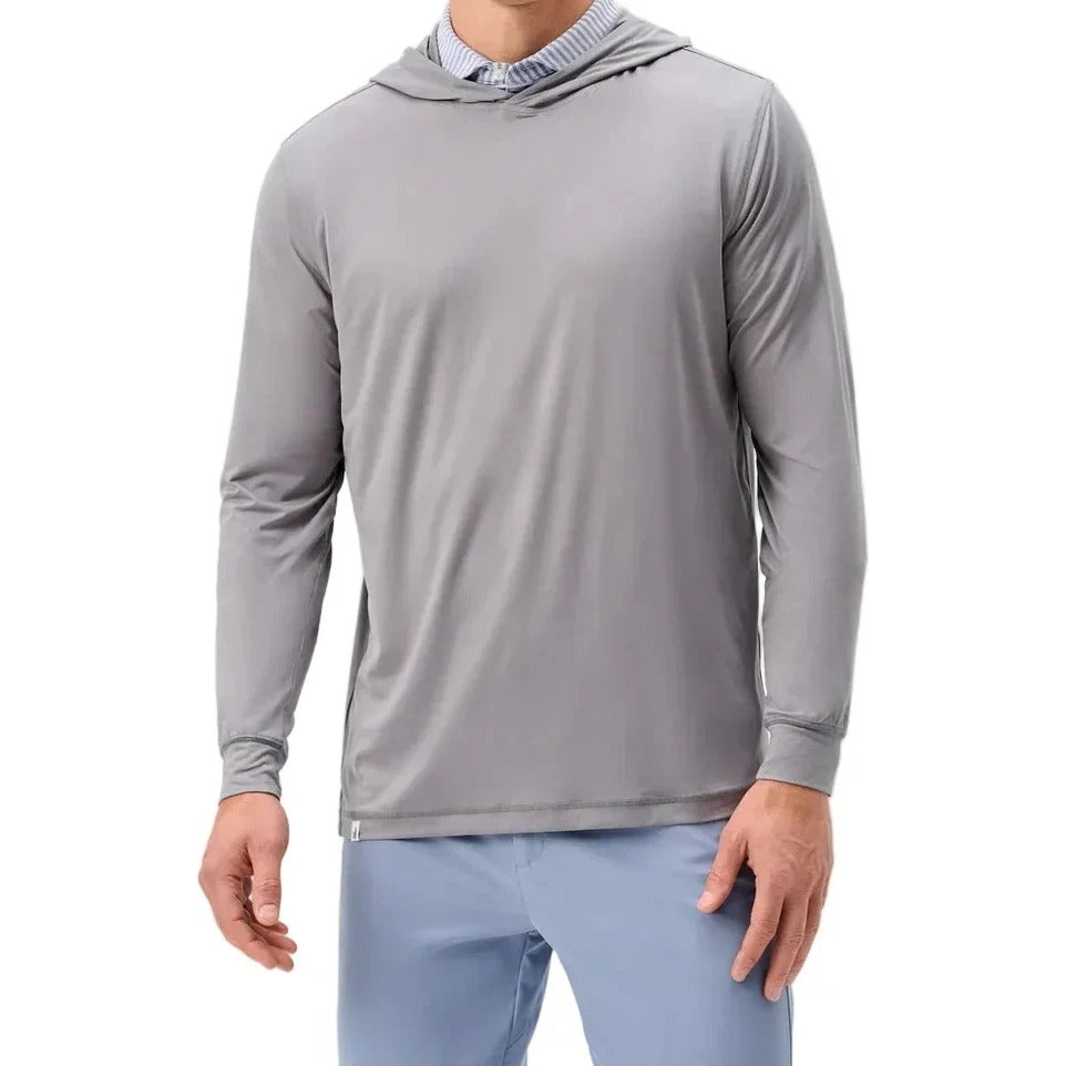A man wearing a light gray long-sleeve performance hoodie over a blue striped collared shirt and light blue pants, photographed against a plain light gray studio background.