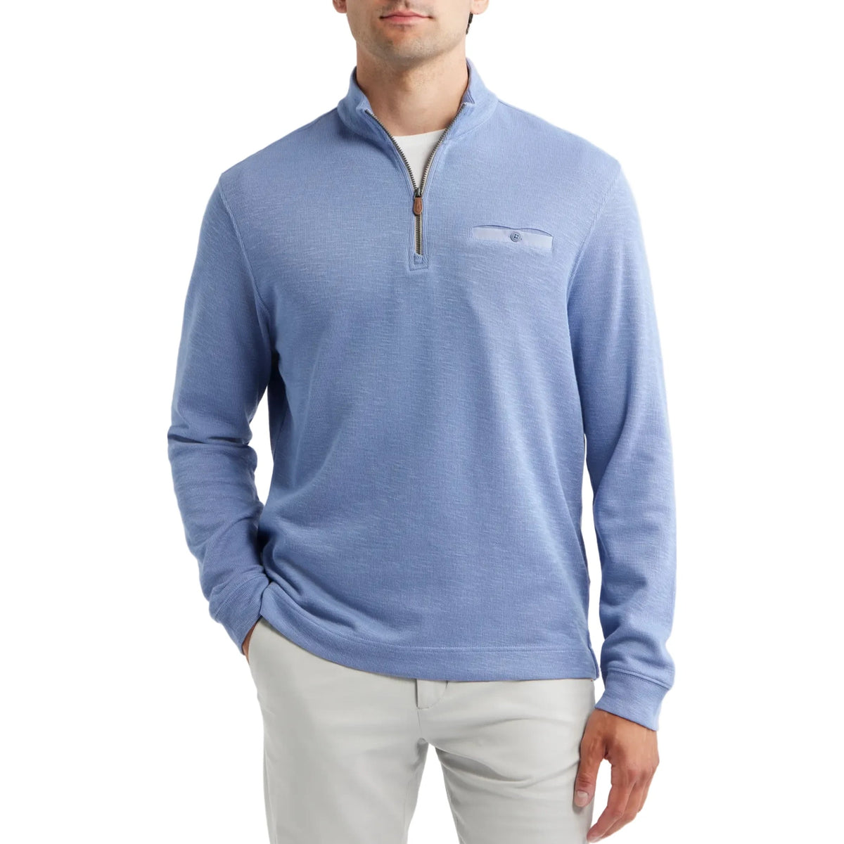 A man wearing a light blue quarter-zip knit sweater with a chest pocket, paired with light gray trousers, against a plain light gray background.