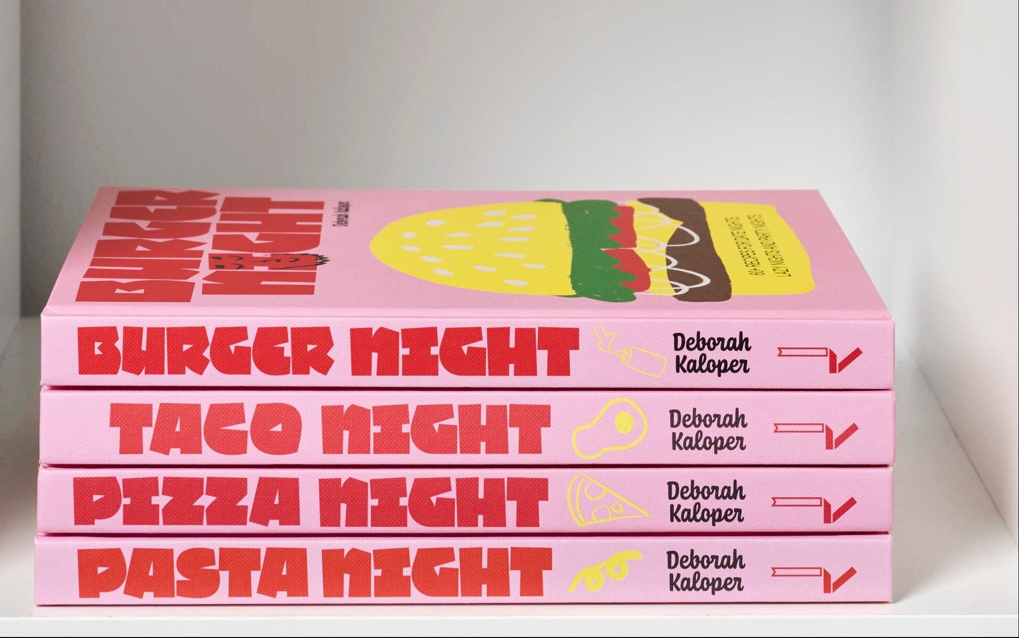 Stack of books titled 'Burger Night', 'Taco Night', 'Pizza Night', and 'Pasta Night' on a white shelf.