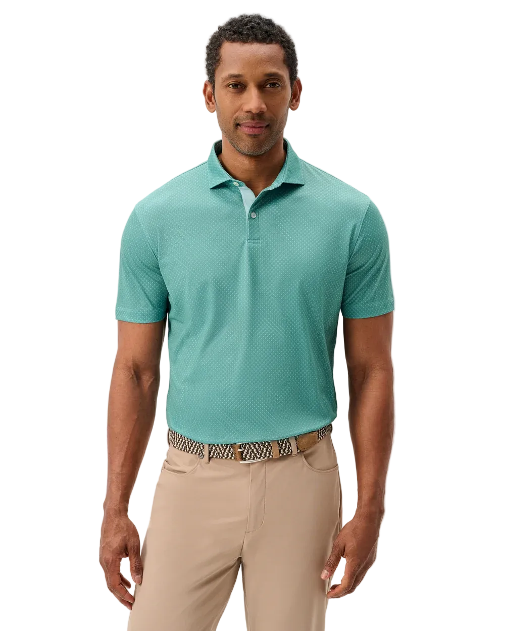 A man wearing a short-sleeve polo shirt in a muted teal-green color, paired with beige trousers and a patterned belt, standing against a light gray studio background.