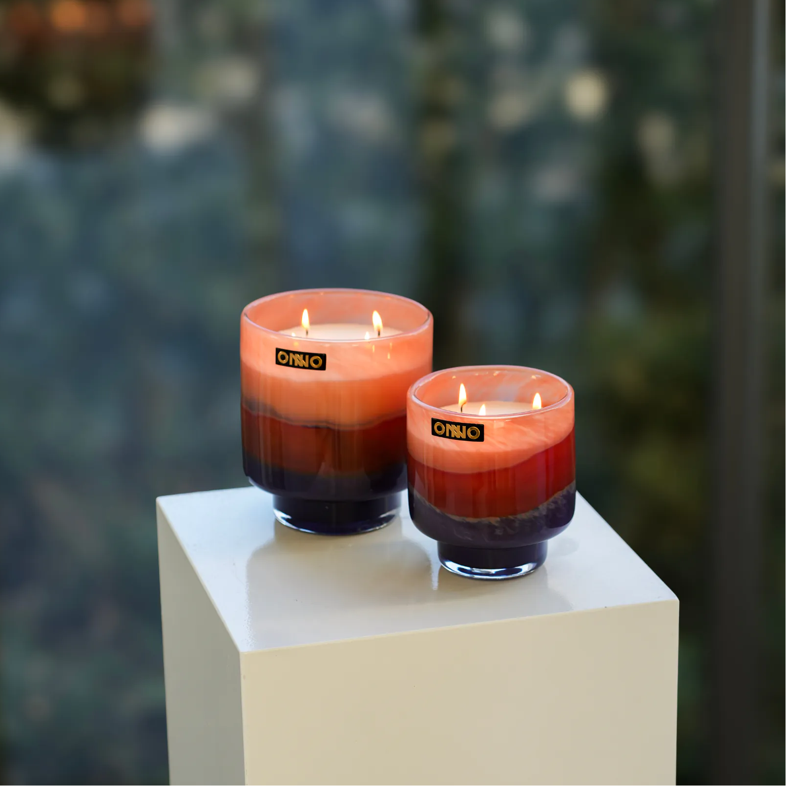 Two gradient candles on a white pedestal with a blurred green background