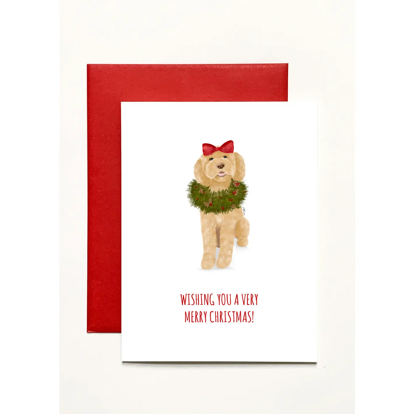 A Christmas greeting card featuring a watercolor illustration of a golden dog wearing a green wreath and red bow, with the text 'WISHING YOU A VERY MERRY CHRISTMAS!' below. The card is shown with a red envelope behind it on a light background.