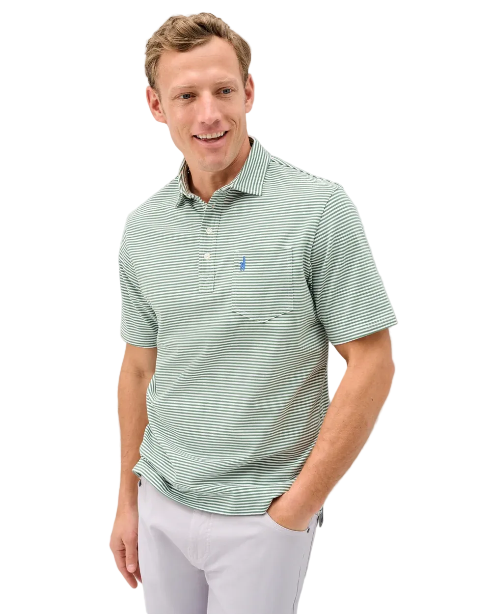 A man wearing a light green and white striped short-sleeve polo shirt with a small blue embroidered logo on the chest, paired with white trousers, standing against a light gray wall.