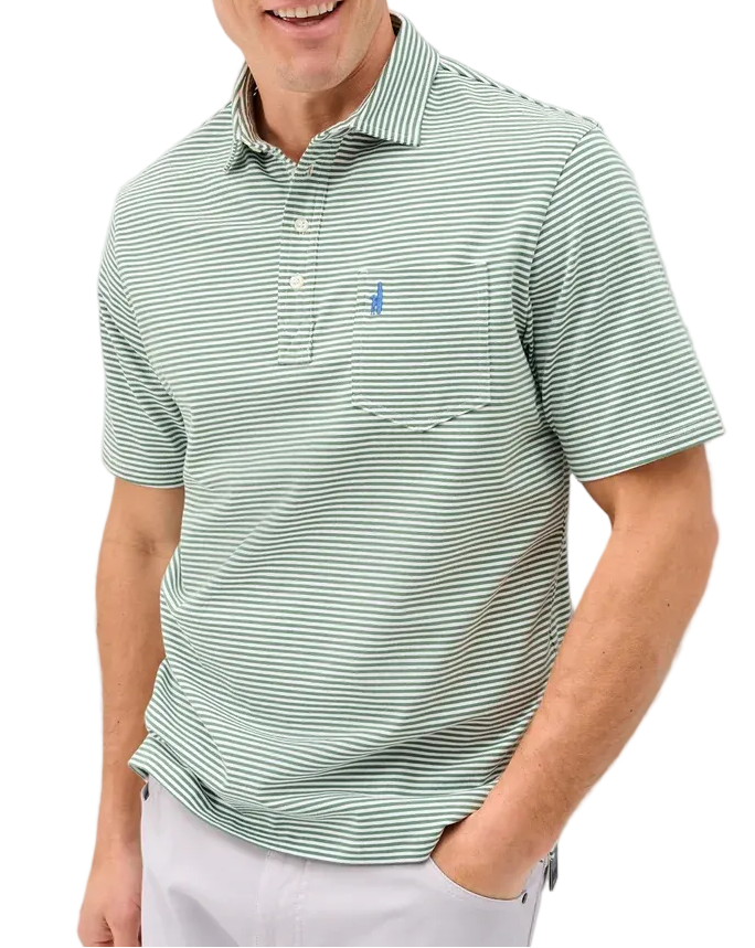 A man wearing a light green and white striped short-sleeve polo shirt with a small blue embroidered logo on the chest, paired with white trousers, standing against a light gray wall.