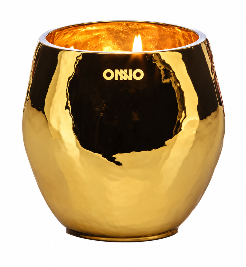 A gold metallic candle holder with a hammered texture, featuring the brand name 'ONNO' printed in gold on the front. The candle is lit inside, casting a warm glow, and is set against a solid white background.