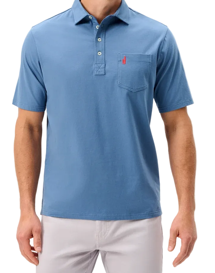 A man wearing a light blue short-sleeve polo shirt with a three-button placket and a chest pocket, paired with light gray trousers, against a plain light gray background.