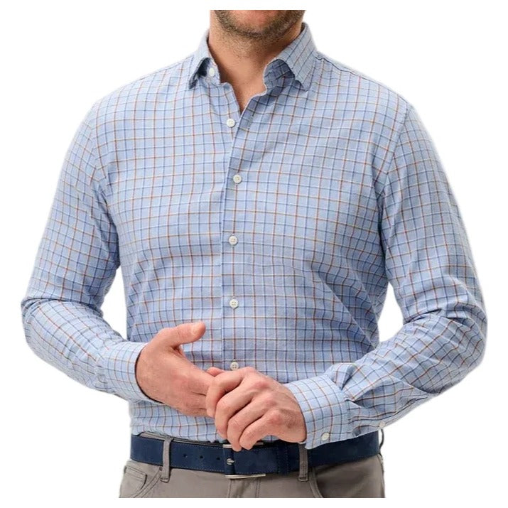 A smiling man wearing a light blue and white checkered long-sleeve button-down shirt, gray trousers, and a dark blue belt, standing against a light gray studio background.