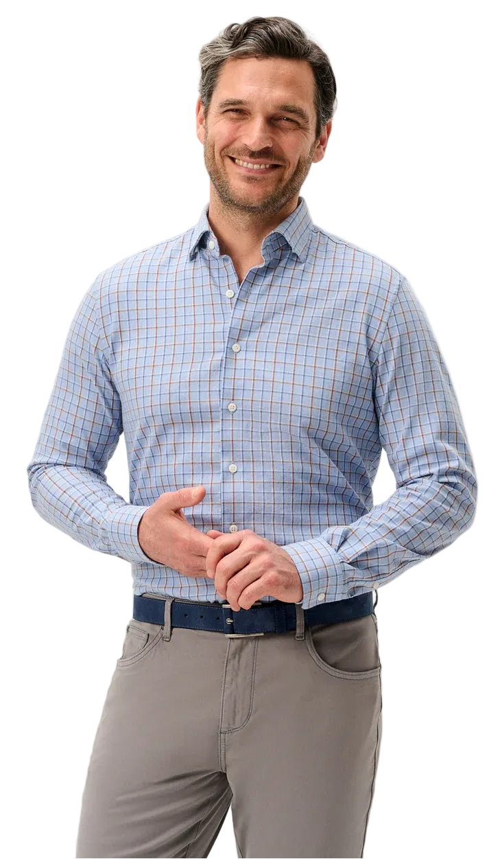 A smiling man wearing a light blue and white checkered long-sleeve button-down shirt, gray trousers, and a dark blue belt, standing against a light gray studio background.