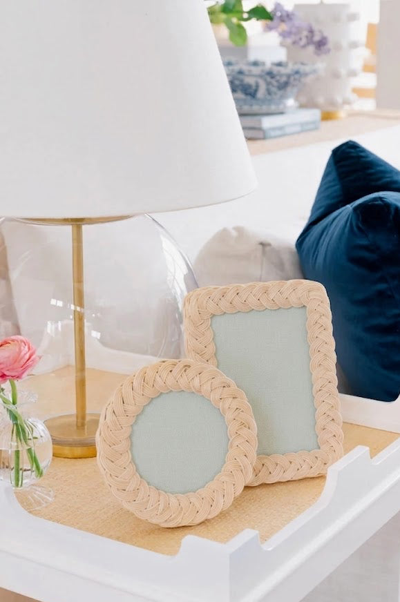 Two round woven picture frames on a table with a lamp and flowers in the background.
