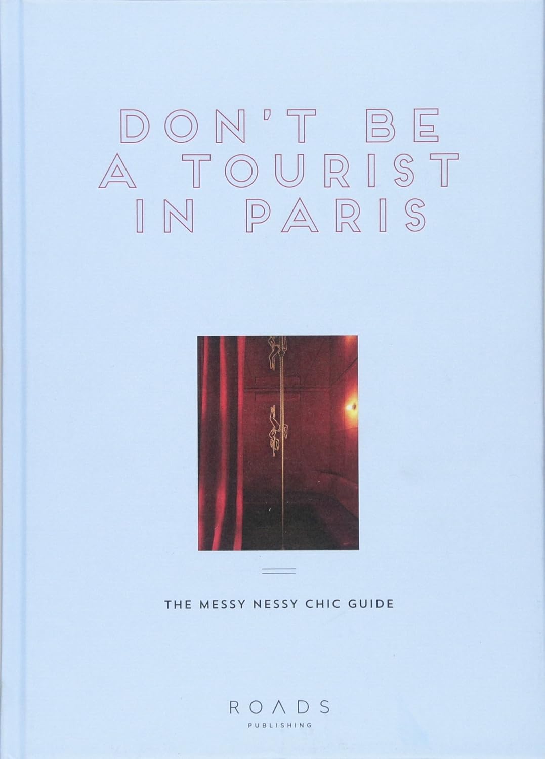 Book cover of 'Don't Be a Tourist in Paris' with a red door illustration on a light blue background.