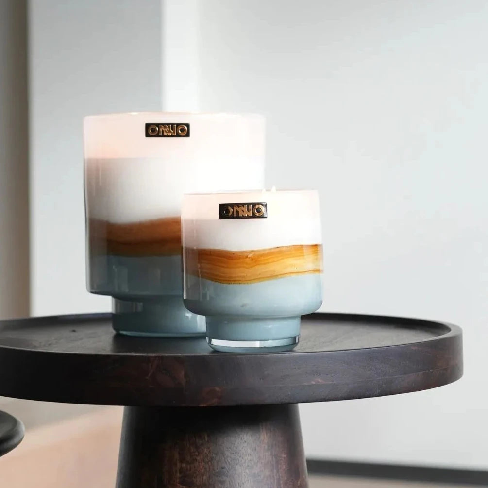 Two candles with gradient design on a small round wooden table.